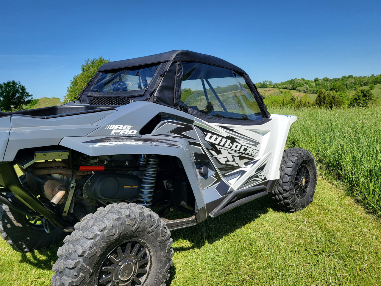 Rear three-quarter view of a white Arctic Cat Wildcat XX with the 3 Star full cab enclosure in tall grass