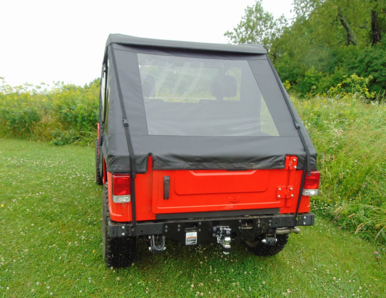 3 Star black soft bed cover with clear rear window on a red Mahindra Roxor, rear view in a grassy field
