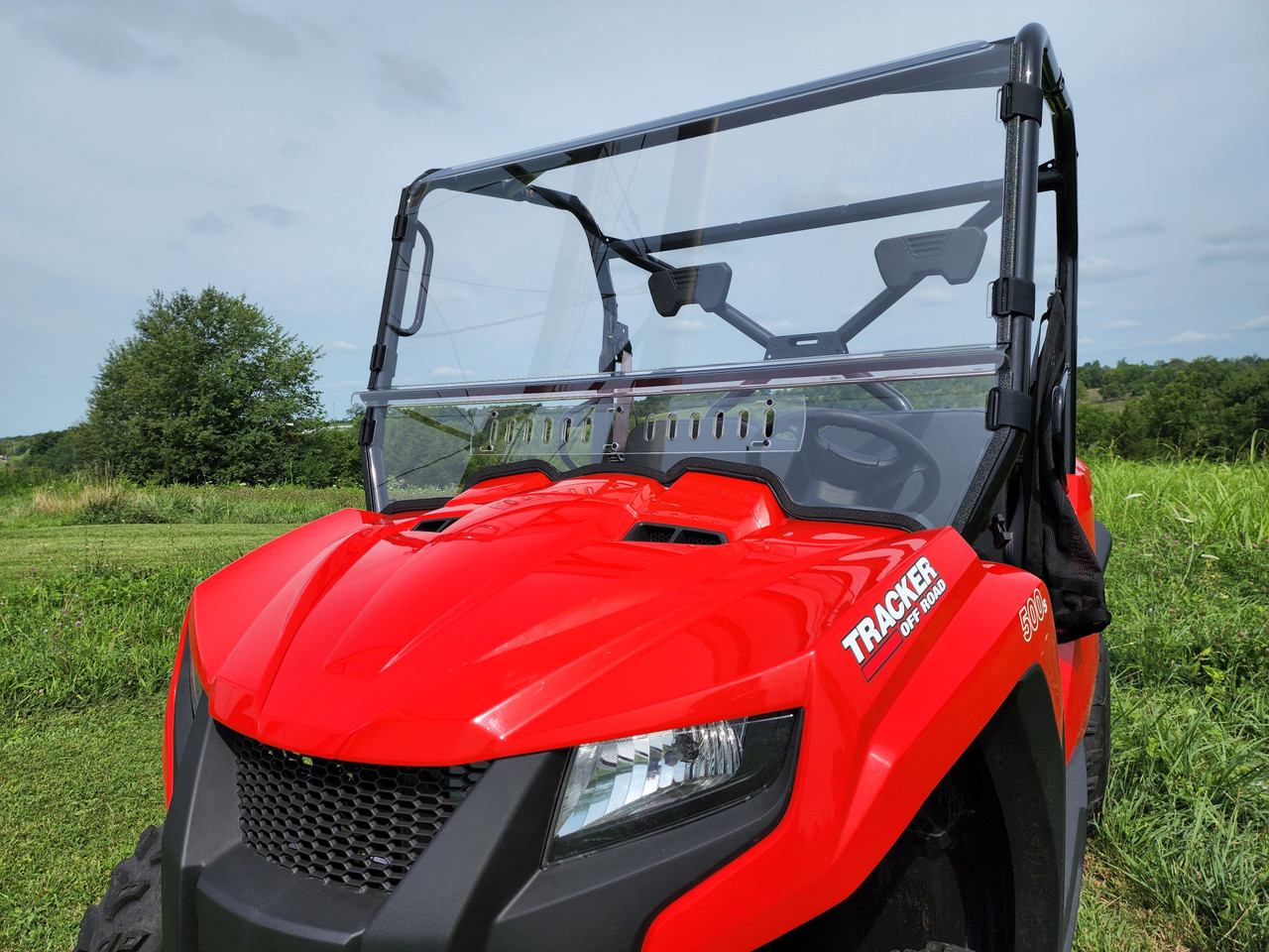 3 Star two-piece windshield on a red side-by-side, front three-quarter view over the hood in a field