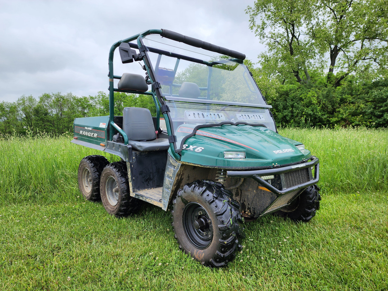 Front three-quarter view of a green six-wheel Polaris Ranger in a field with the 3 Star two-piece windshield