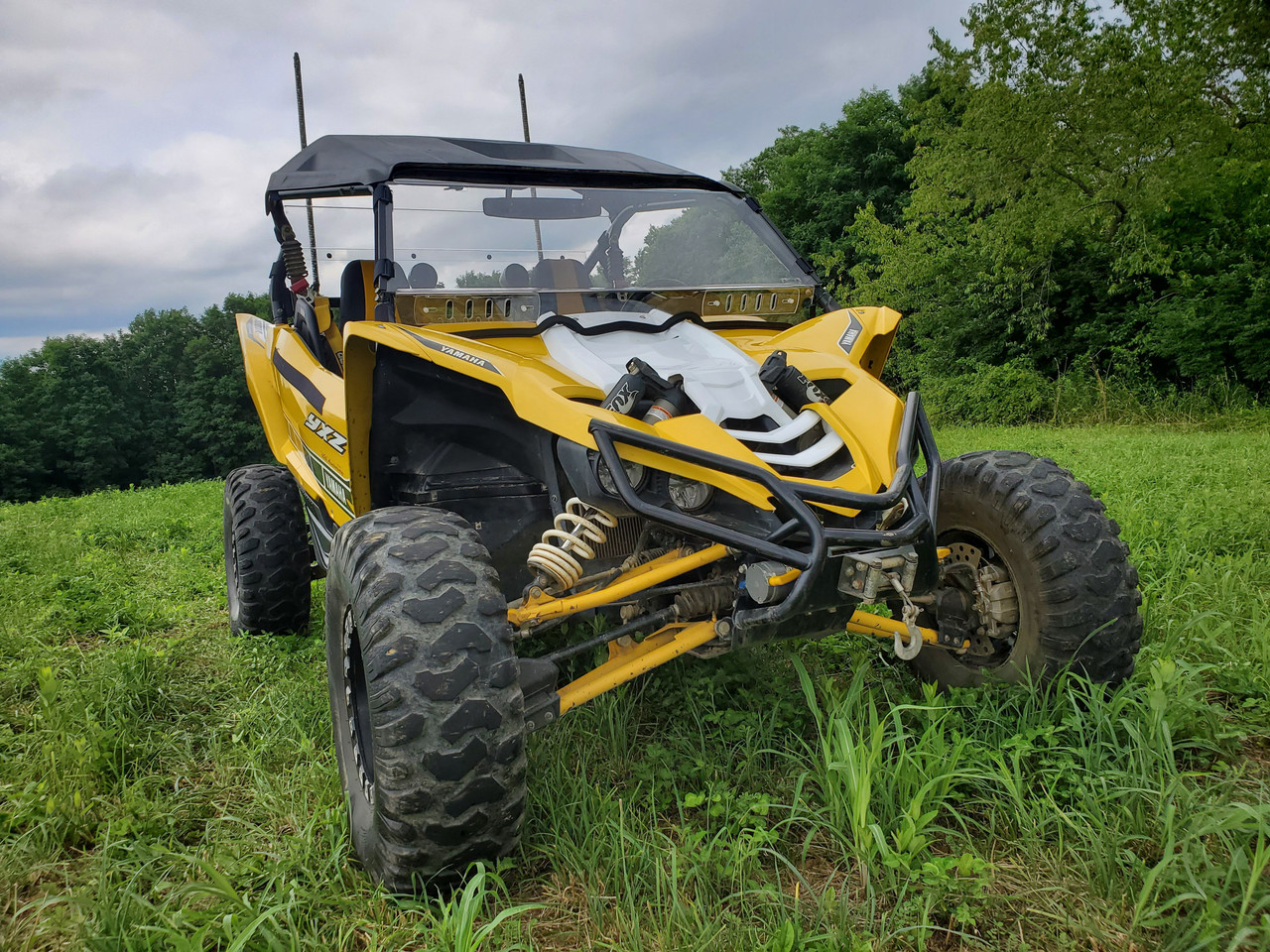 3 Star one-piece windshield on a yellow Yamaha YXZ with soft top, front three-quarter view in tall grass