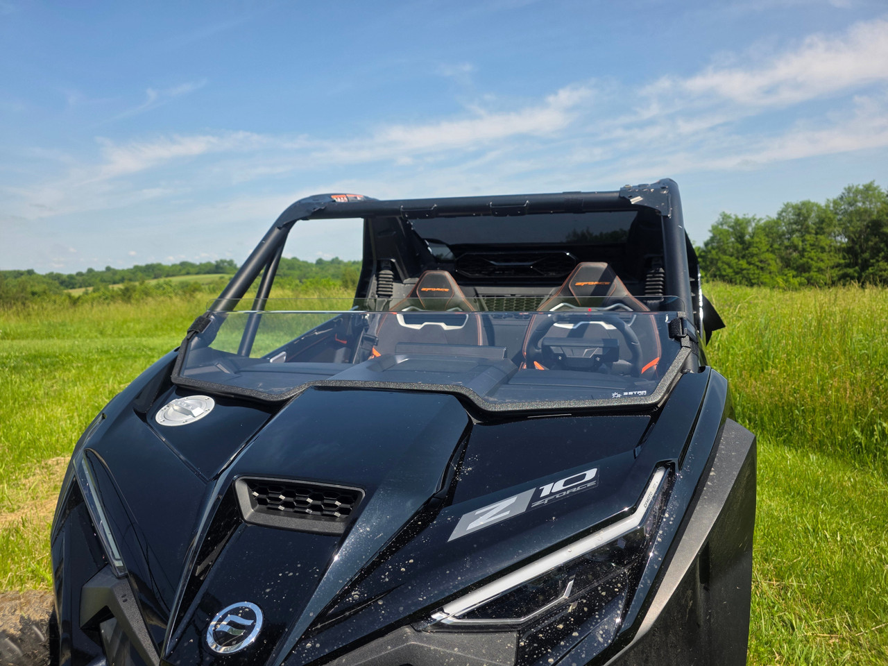 3 Star clear polycarbonate half windshield installed on a black CFMoto ZForce Z10, front view over the hood in a field