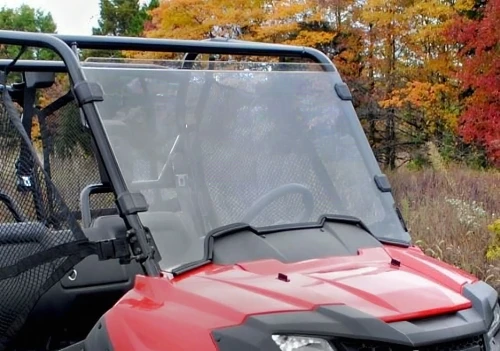 SuperATV full windshield installed on a red Honda Pioneer 700 with fall foliage behind, front three-quarter view