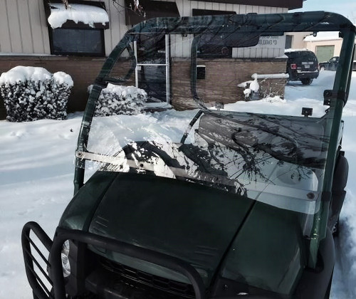 Extreme Metal Products clear hard windshield installed on a green Kawasaki Mule 600/610, front view over the hood in snow
