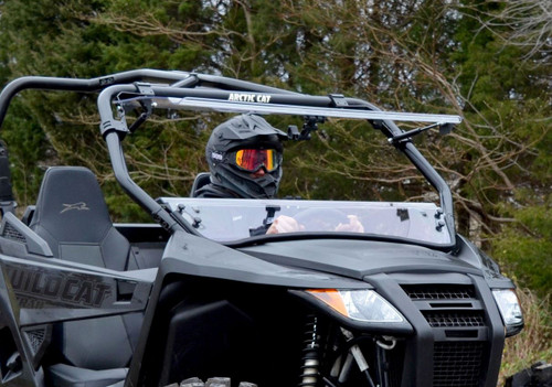 SuperATV flip-up windshield with the top half open on a black Arctic Cat Wildcat Trail, helmeted driver at the wheel
