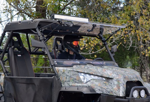 SuperATV flip-up windshield installed on a camo Odes Dominator, front three-quarter view with the windshield closed