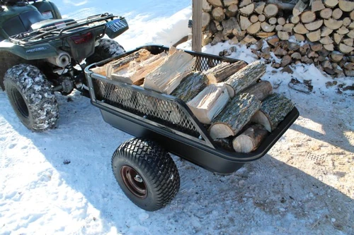 Moto Alliance Impact Implements off road trailer with mesh side rails loaded with firewood, hitched to an ATV in snow