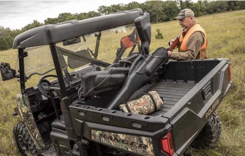 Kolpin in-bed double gun boot mount holding two gun boots in the cargo bed of a camo side-by-side, hunter standing behind