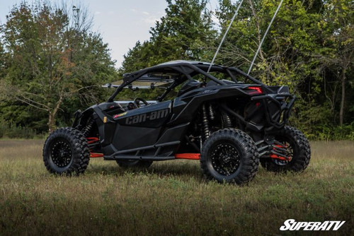 Front three-quarter view of the black Maverick X3 with SuperATV nerf bars, parked on grass with trees behind