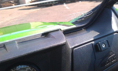 Close-up of the Extreme Metal Products hard windshield lower edge meeting the dash of the green Arctic Cat Wildcat 1000