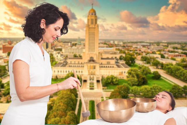 Vibrational Sound Therapy practitioner playing singing bowls for a client on a massage table, Lincoln, NE skyline
