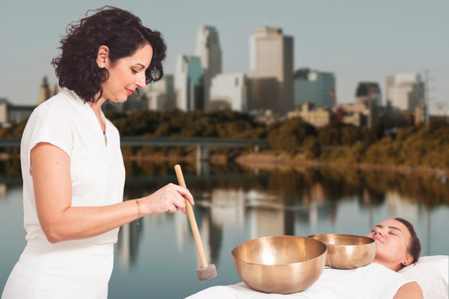 Vibrational Sound Therapy practitioner playing singing bowls for a client on a massage table, Minneapolis, MN skyline