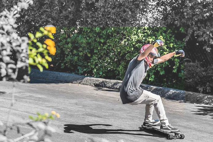 Skateboarder carving on a paved road surrounded by green vegetation