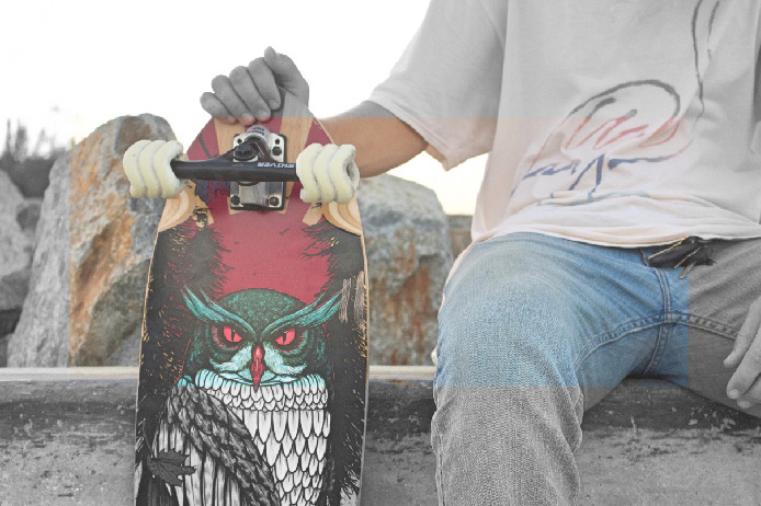 Person holding a skateboard with light-colored wheels beside rocks and trees