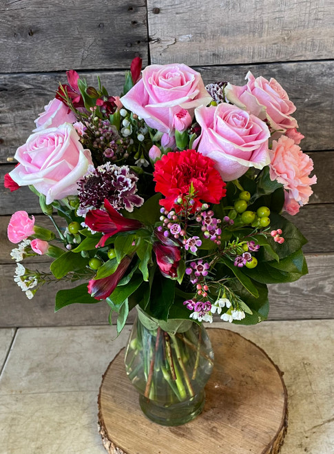 Pink roses, red and pink carnations, alstromeria, and hypericum berries in a vase with fresh seasonal accents in a glass vase.