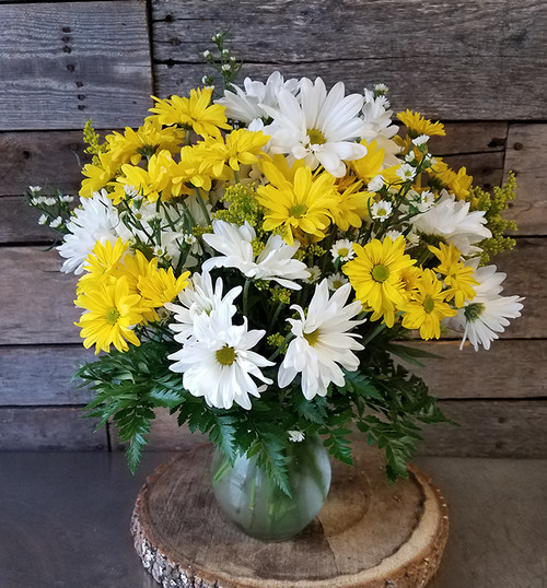 a mix of white and yellow daisies with matching filler and greenery in a clear glass vase