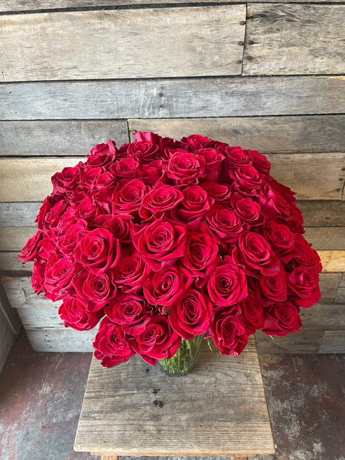 One hundred velvety long stemmed red roses arranged snugly in a large vase.