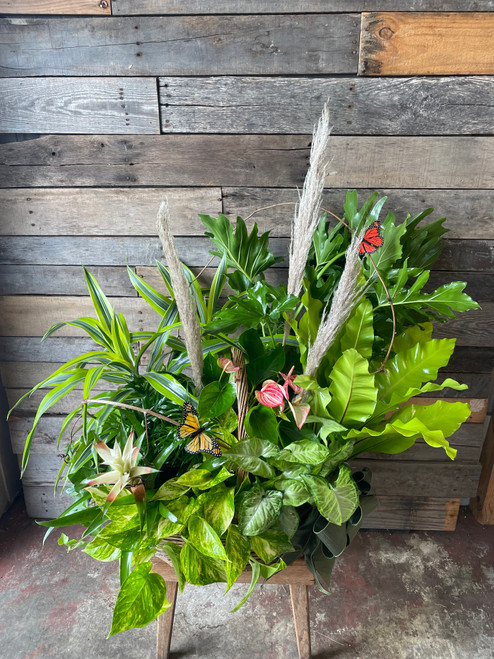 A large basket filled with a variety of green plants, cut flowers, and dried elements.