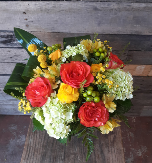 a low and lush arrangement with orange roses, yellow and green filler, with mini green hydrangeas in a low clear glass vase