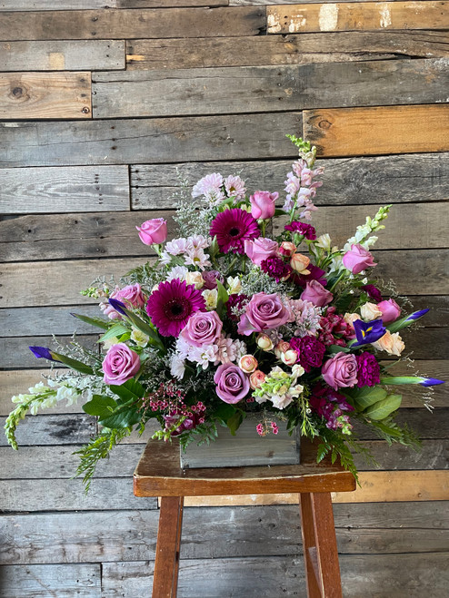 A large pyramid arrangement full of lavender roses, daisies, and a mix of purple and violet seasonal flowers