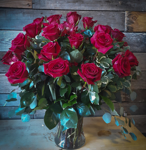 thirty long stemmed red roses in a large clear vase with complimenting greenery