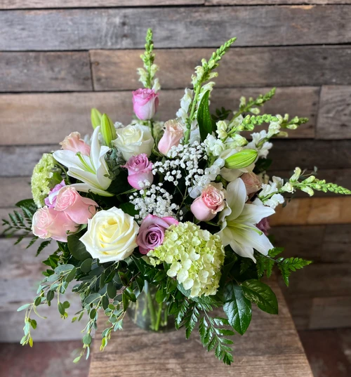 Arrangement features classic roses and spray roses surrounded by hydrangea, chrysanthemums, alstroemeria, hypericum berries, and fresh greenery in a glass vase.