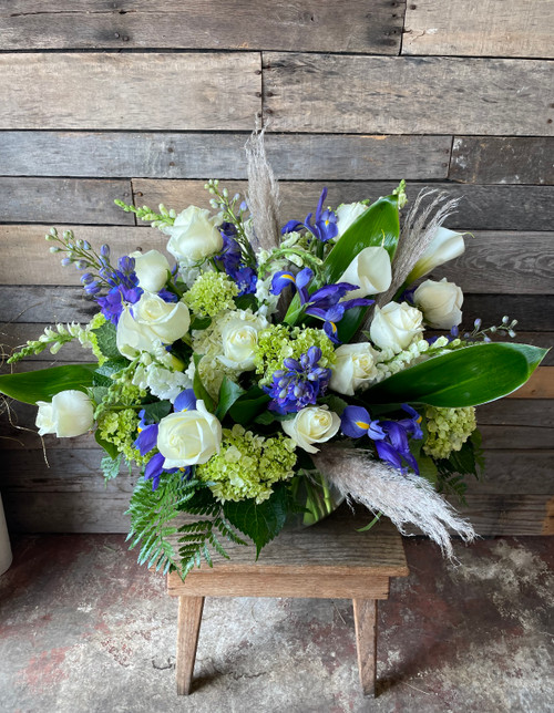 A low and lush arrangement filled to the brim with white roses, green hydrangeas, blue iris, and dried elements.