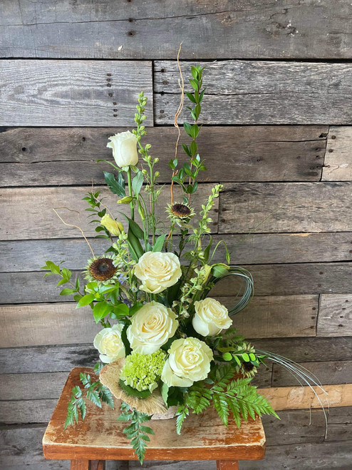 A unique arrangement showcasing white roses, sunflower centers, green hydrangeas, snapdragons, with seasonal greenery in a rectangle dish.