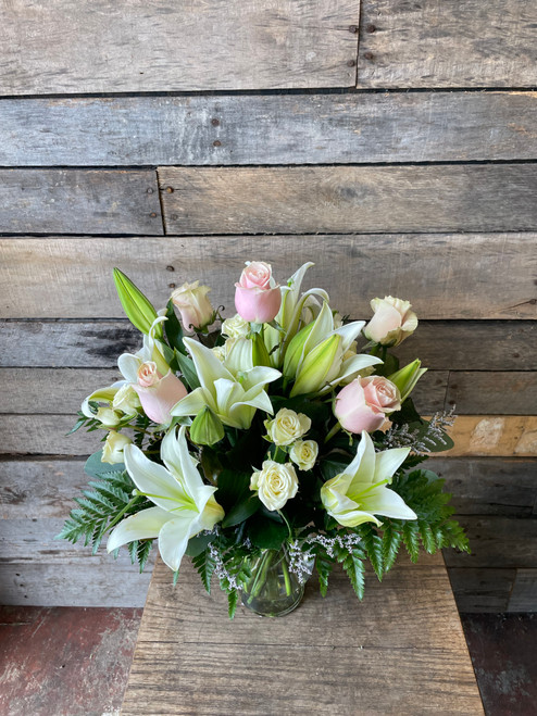 Pink roses, white spray roses, white lilies, seasonal greenery, arranged in a glass vase