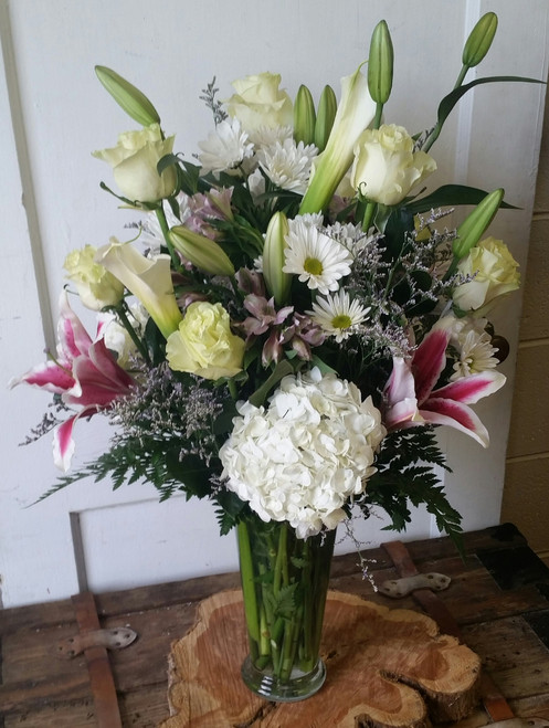 This classic garden style vase arrangement is full of white roses, daises, hydrangea, and stargazer lilies arranged in a clear glass vase.  