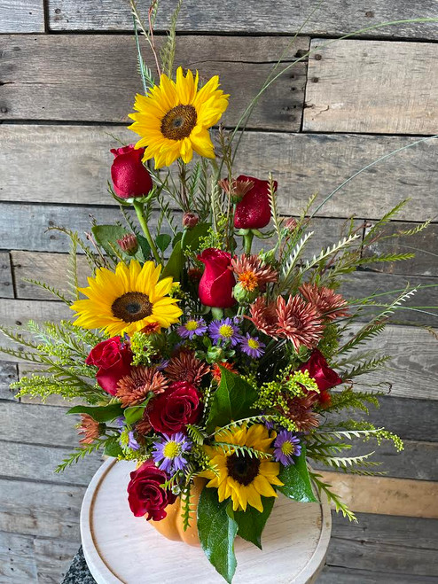 Red roses, sunflowers,  chrysanthemums, bells of ireland, solidago, and fresh seasonal greenery in a pumpkin shaped container.