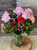 Pink roses, red and pink carnations, alstromeria, and hypericum berries in a vase with fresh seasonal accents in a glass vase.