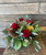 A low and lush arrangement with winter greenery, pinecones, red roses, and dried citrus