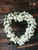 Heart-shaped funeral wreath filled with white roses, white spray roses, white carnations, and seasonal green foliage.