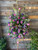 A traditional shield shaped standing spray with a mixture of fuchsia, lavender, and deep purple seasonal flowers with a complementing bow in the middle.