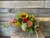 Sunflowers, chrysanthemums, hypericum berries, solidago, snapdragons, with fresh seasonal greenery in a pumpkin shaped vase.