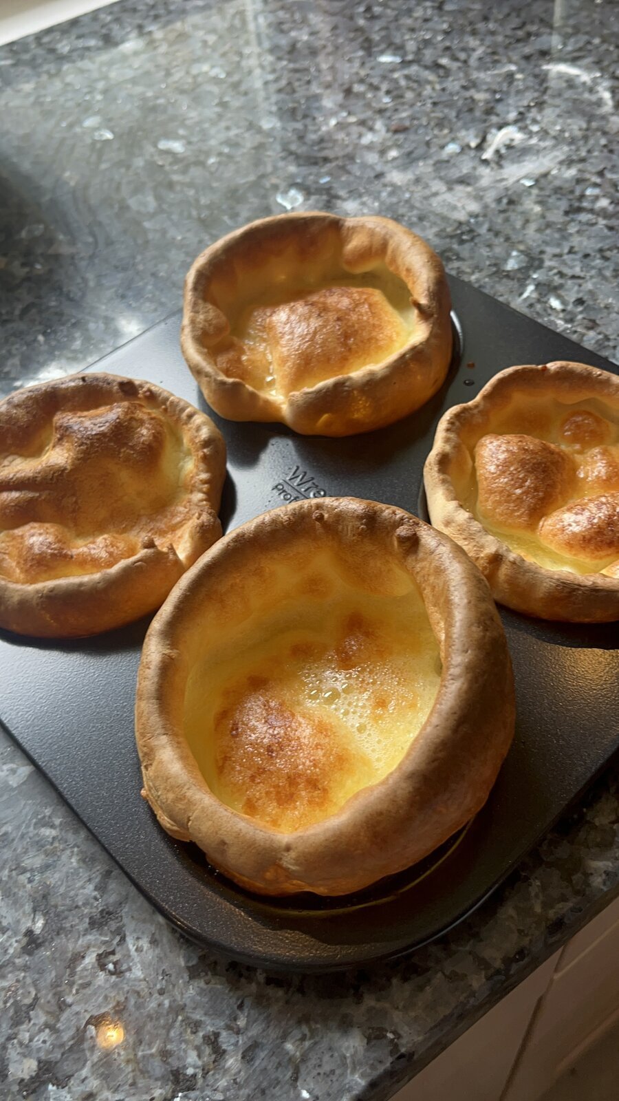 Tall golden Yorkshire puddings risen above a Wrenbury 4-cup carbon steel tray on a kitchen surface