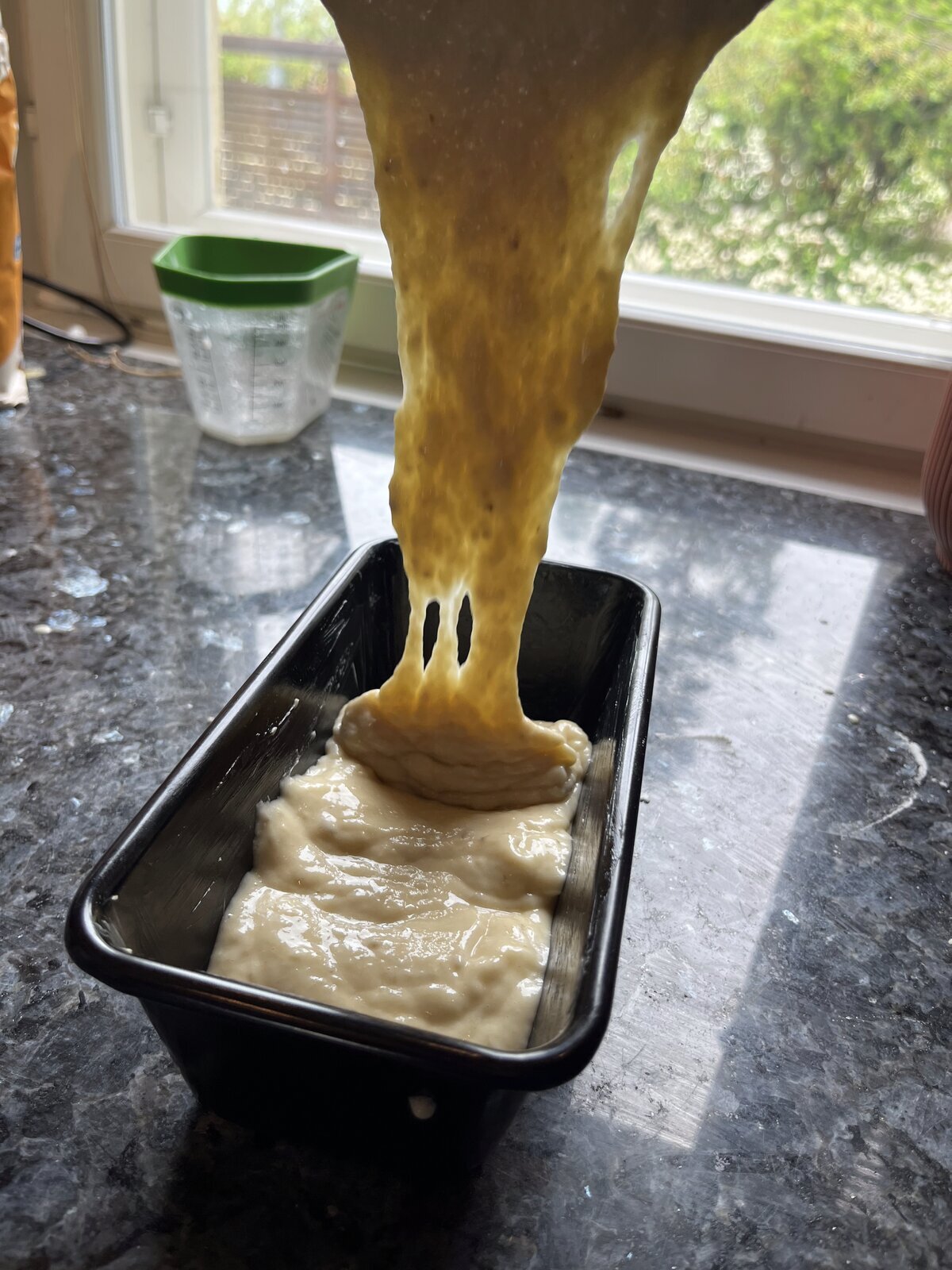 Banana bread batter being poured into a greased 1lb loaf tin