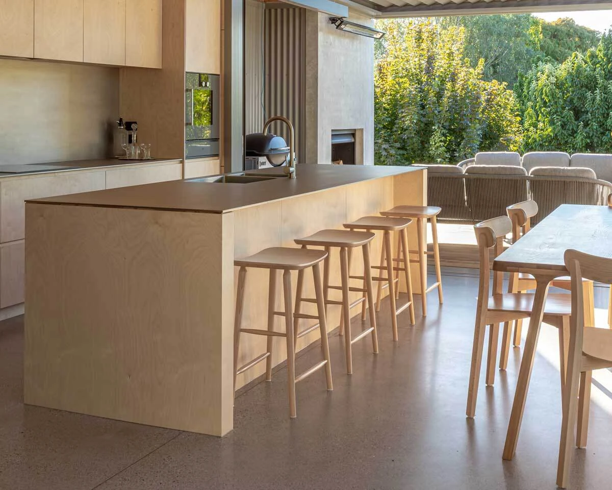 Natural Mackenzie timber bar stools with curved seats, styled along a modern kitchen island in an open-plan living space.