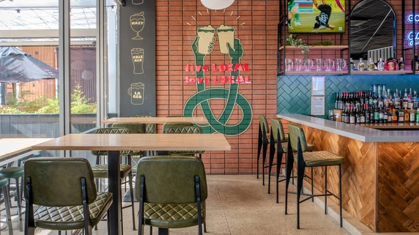 Dave bar stools with olive green upholstered seats and black metal legs, lined along the bar in a contemporary hospitality venue.