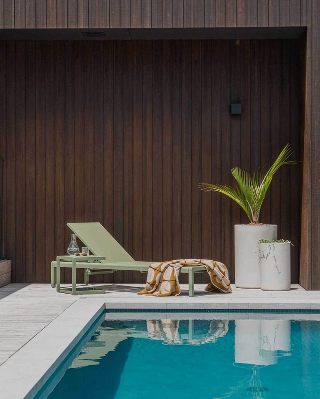 green matakana sun lounger sitting beside a bright blue swimming pool