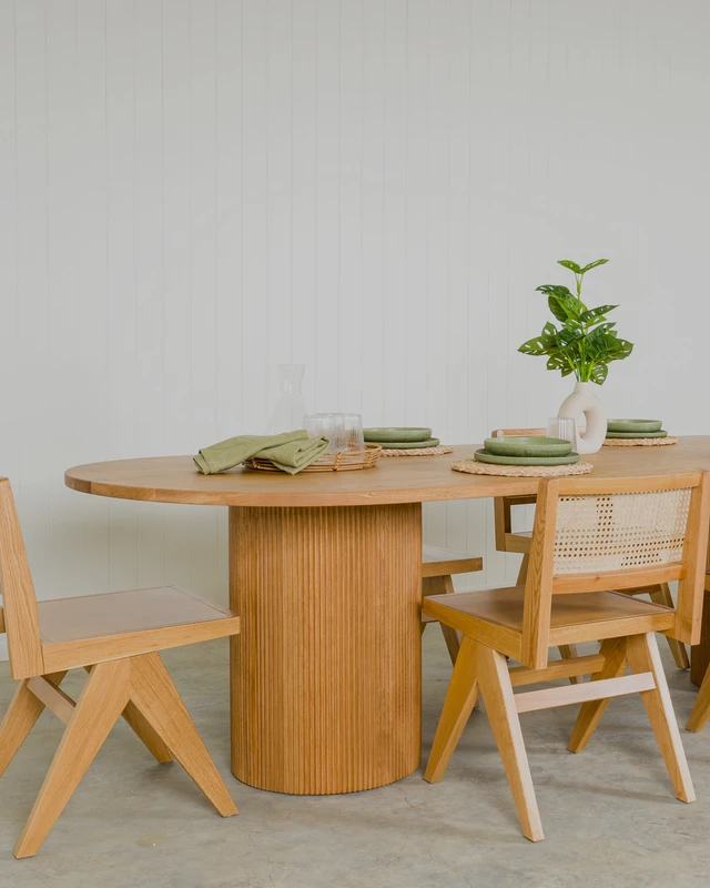 Reid dining table in natural oak with curved top and fluted pedestal legs, surrounded by Lillian oak dining chairs.