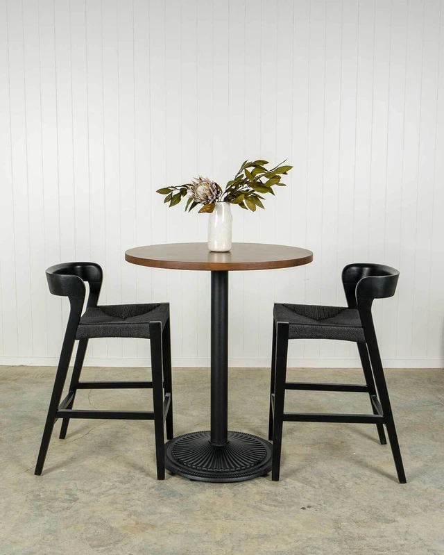 Round solid oak bar leaner table on a black Winifred pedestal base, paired with black Grace rope bar stools with curved backs.