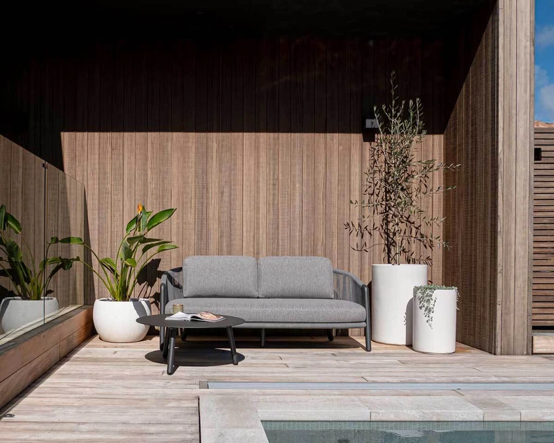 Waiheke outdoor armchairs with light cushions and woven rope detailing, paired with a Piha side table on a timber deck.