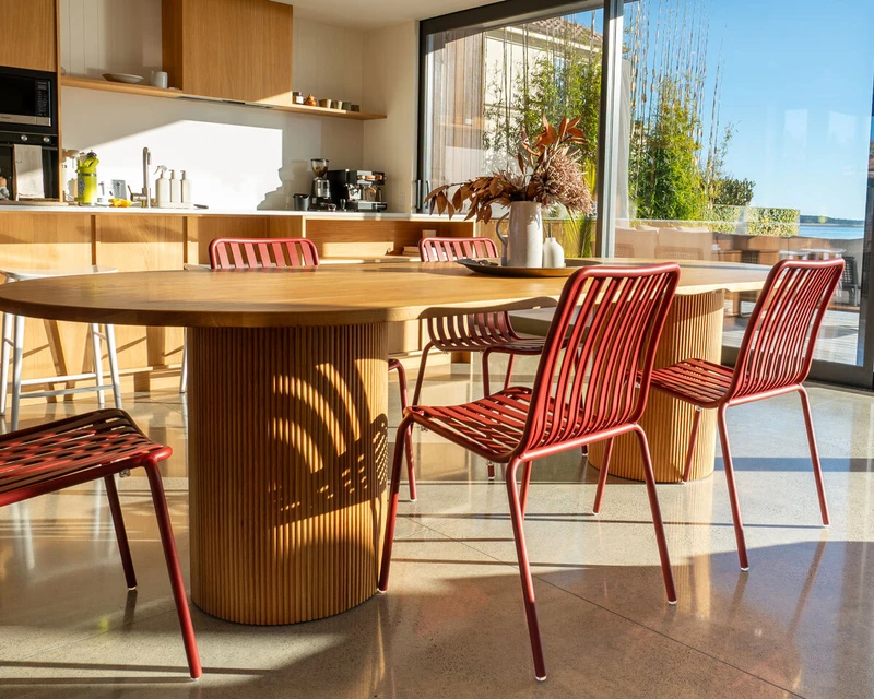 Brick-coloured aluminium Parker dining chairs with slatted seats and backs, paired with the Reid oak dining table featuring rounded edges and fluted pedestal legs.