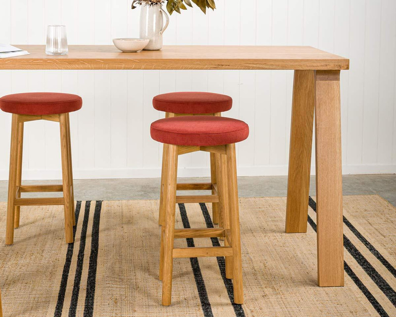 Natural timber stool with a brick upholstered seat at a natural timber bar leaner
