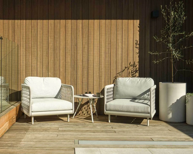 Waiheke outdoor armchairs with light cushions and woven rope detailing, paired with a Piha side table on a timber deck.