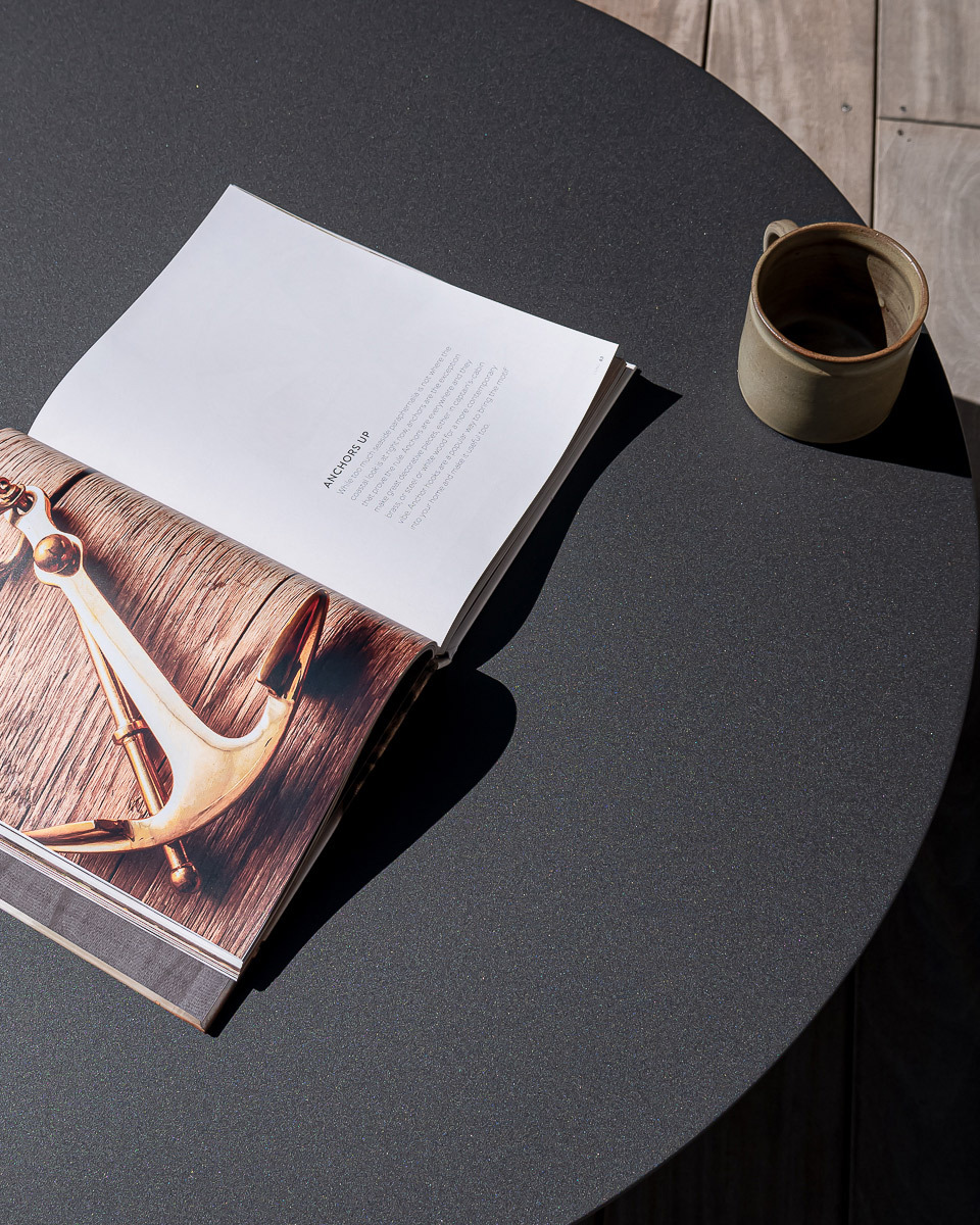 Dark charcoal aluminium outdoor table with book and green coffee cup.