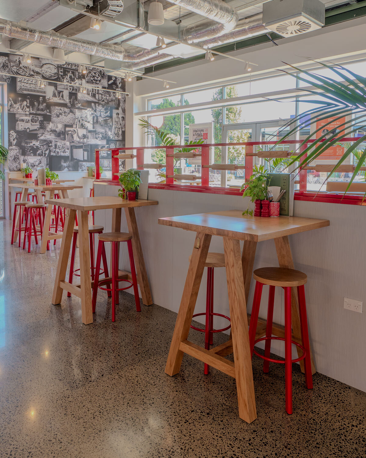 Idaho natural oak bar leaner paired with powder coated red stools in a bar setting.