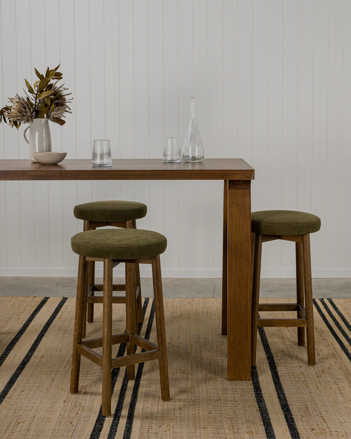 Curve bar stool with dark oak frame with a vibrant olive green fabric seat paired with a dark oak Harrison bar leaner